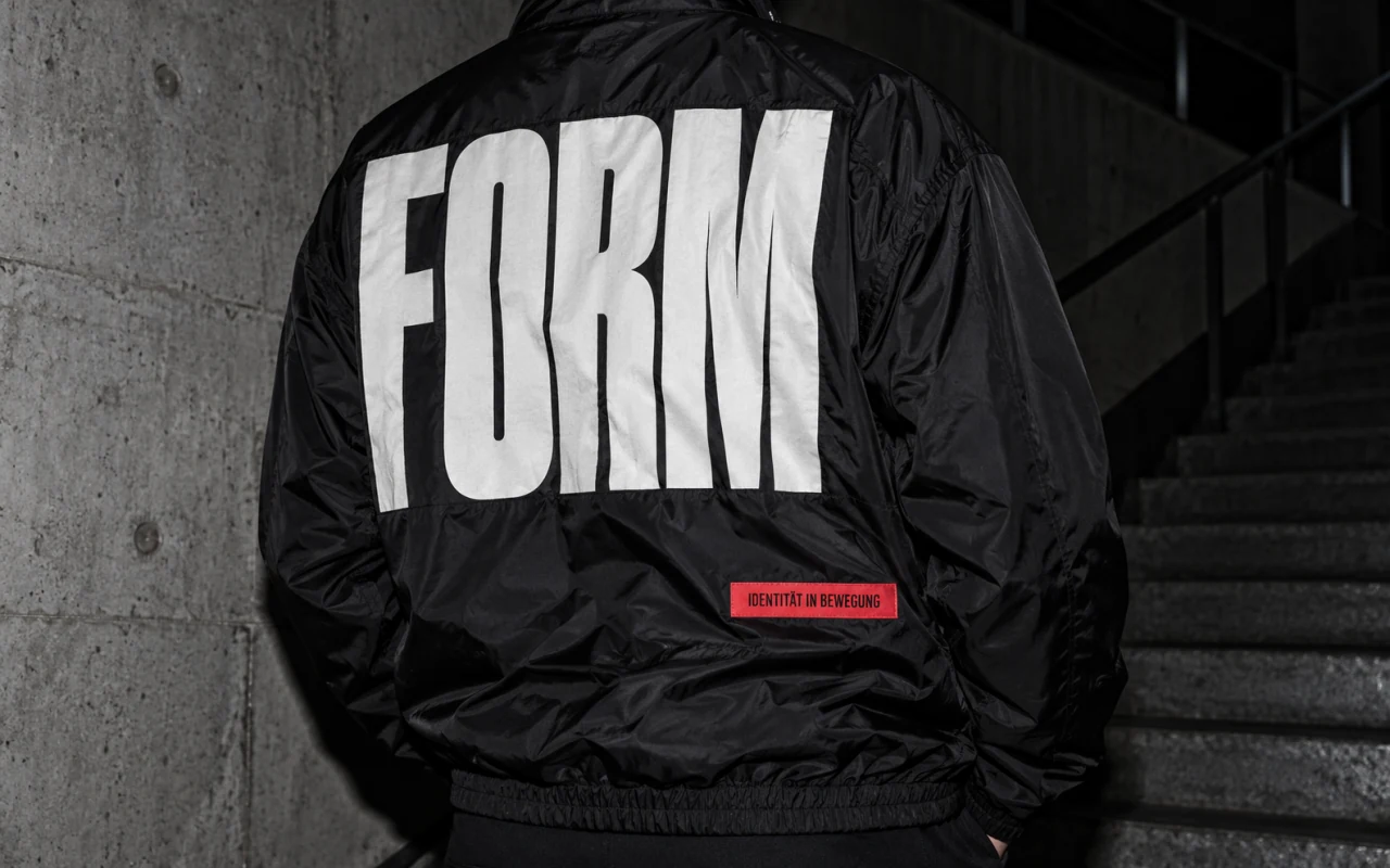 Schwarze Nylonjacke mit großer weißer Form-Typografie und rotem Stofflabel