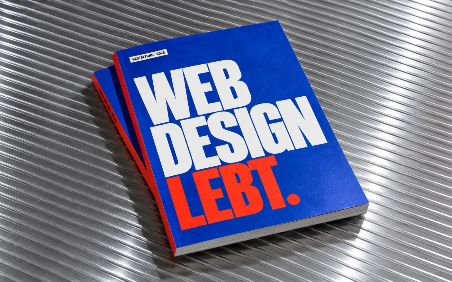 Kobaltblaues Designmagazin mit der Aufschrift Webdesign lebt auf geriffeltem Aluminium