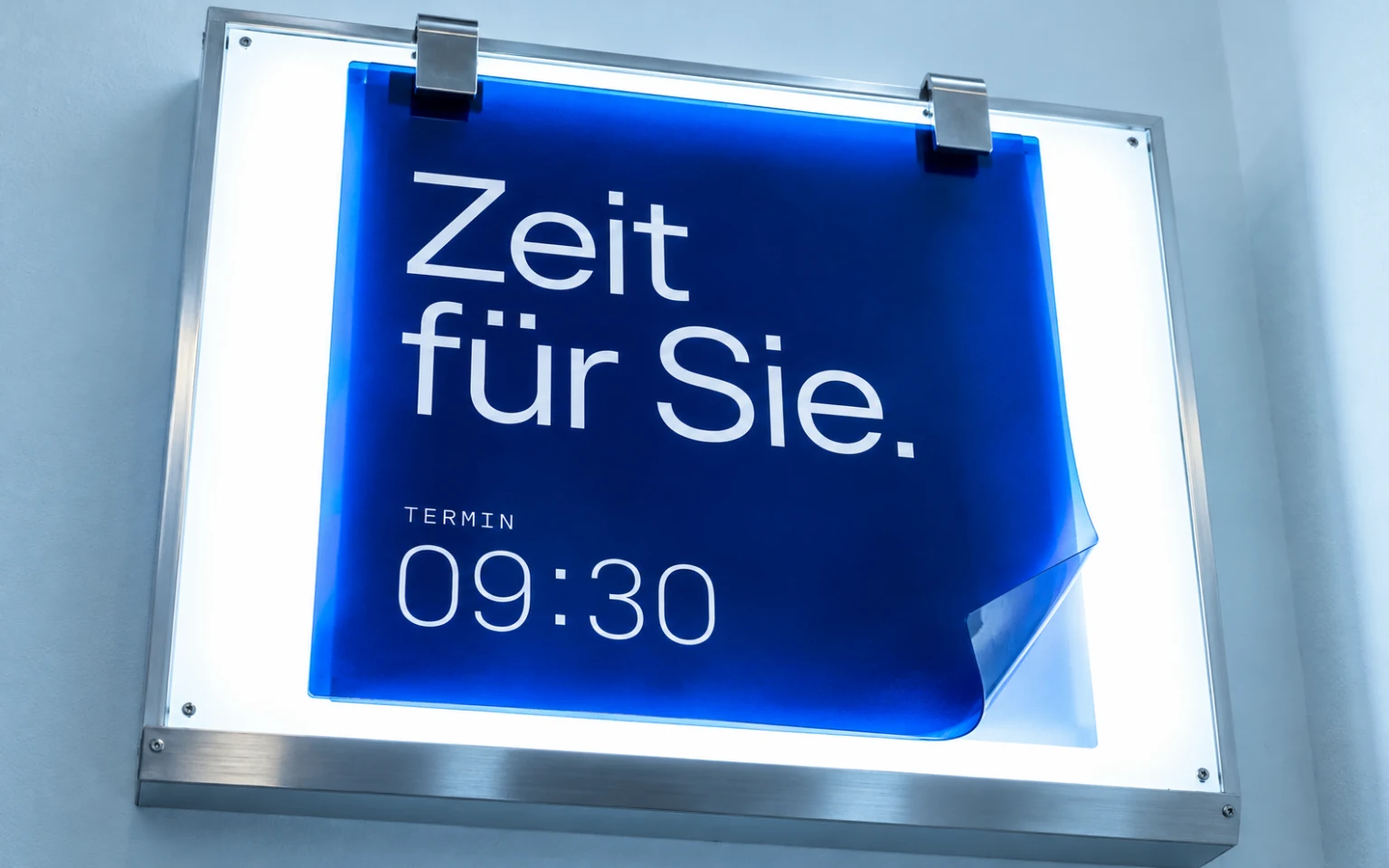 Klinisch beleuchtetes Termin-Display mit transparenter blauer Grafikfolie und dem Schriftzug Zeit für Sie